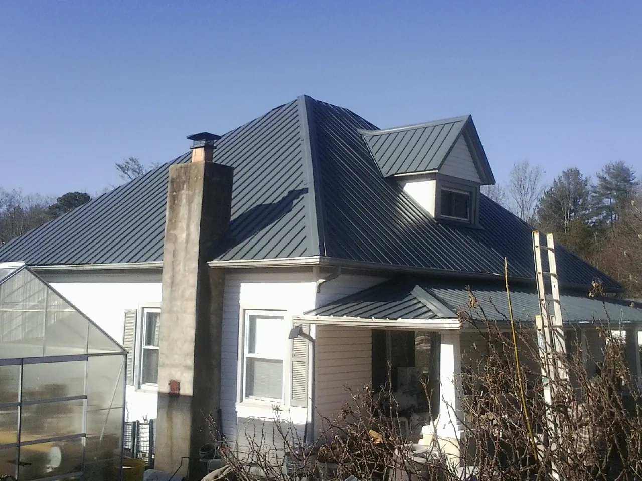 Dark blue standing seam metal roof on a white farmhouse with dormer — Slate & Tile Roof Repair by Roofing Brothers in Elmont