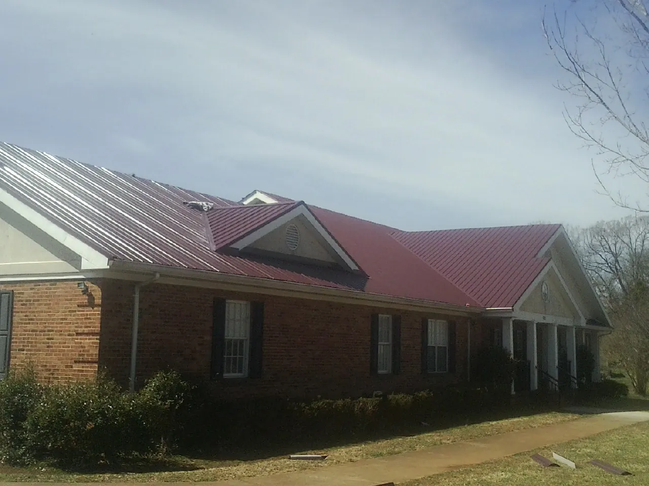 Red metal roof with gabled entries on a long brick building, from a Hail Damage Roof Repair job in Elmont