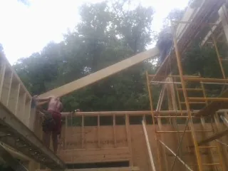 Carpenter raising a rafter beam on a new second story frame in Elmont