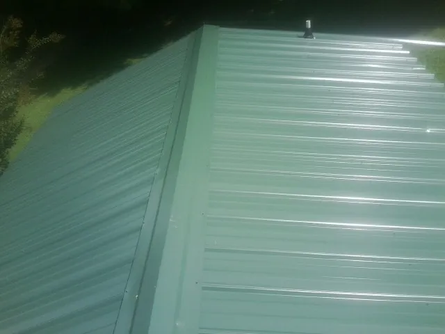 New green metal panels meeting at the ridge of a roof — Flat Roof Repair work by our crew in Elmont