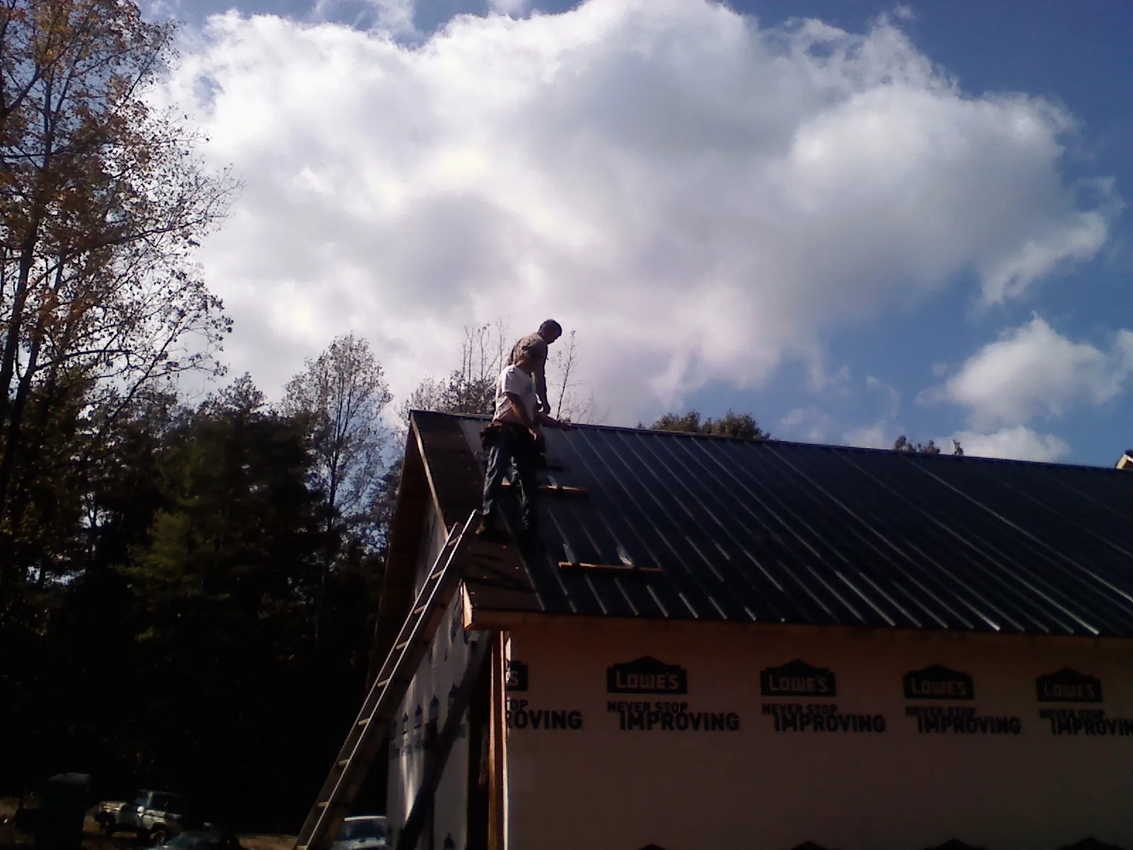 Roofer fastening dark metal panels high against a cloudy sky, from a Roof Inspection job in Elmont