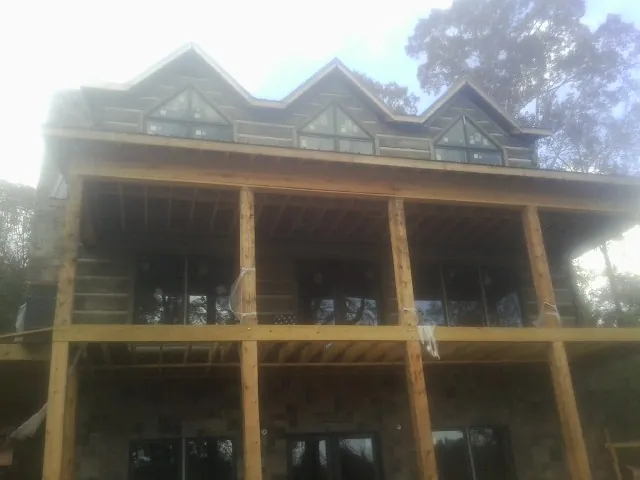 Dormers and porch framing on a large log home under construction — Roof Coating work by our crew in Elmont