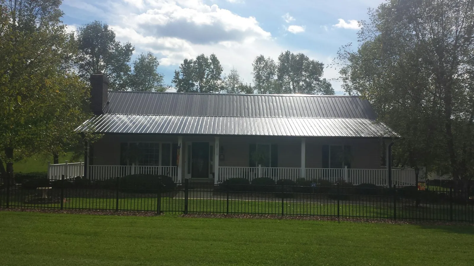 Gray metal roof on a brick ranch with a full width front porch — Gutter Guard Installation work by our crew in Elmont