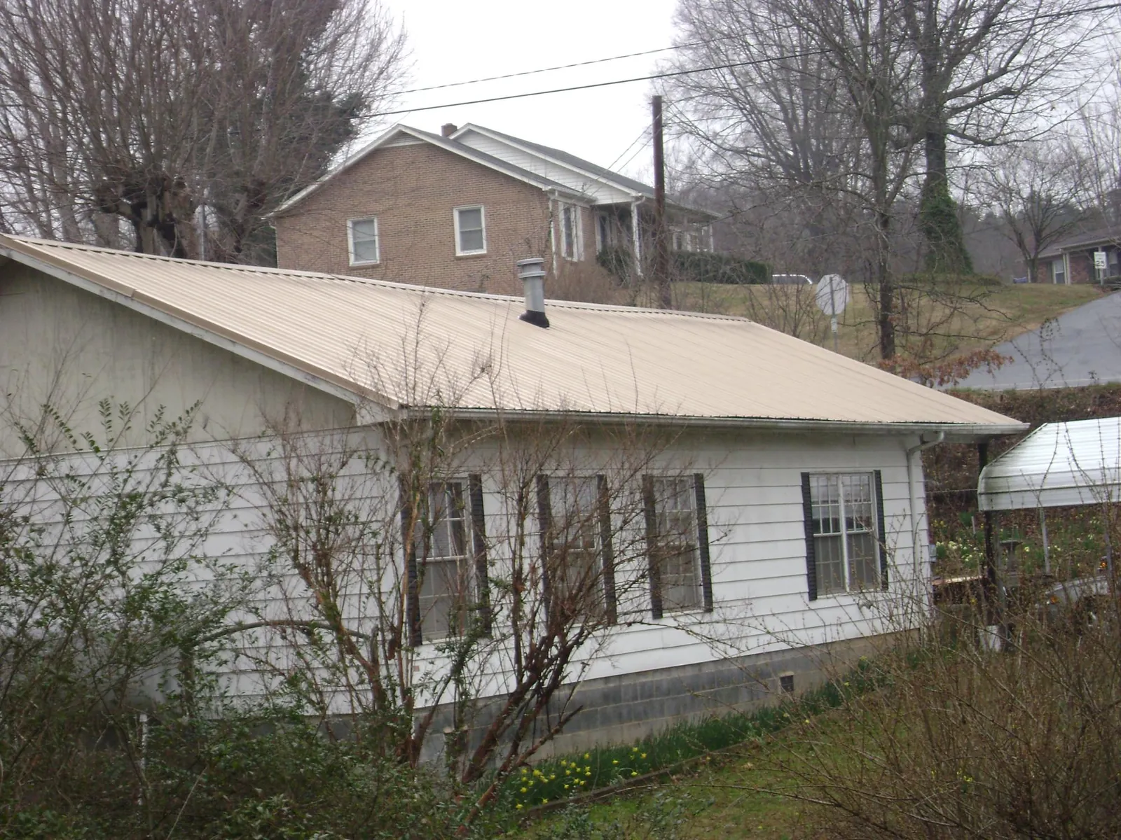 Tan metal roof on a white sided house set into a hillside — Commercial Roofing by Roofing Brothers in Elmont