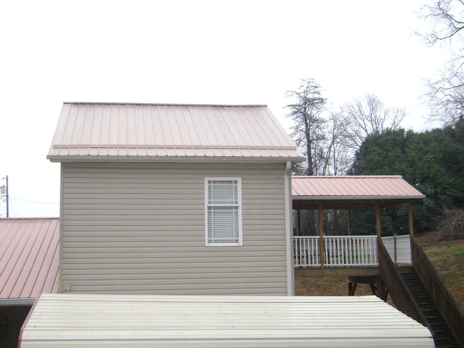 Tan metal roofs on a two story addition and attached porch, from a Roof Replacement job in Elmont